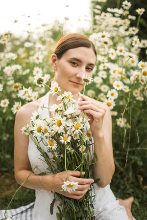 a girl with a large bouquet of daisies sits in natureの写真素材
