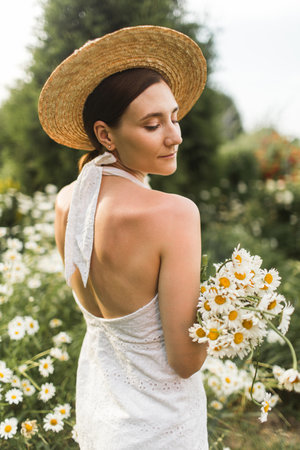 beautiful girl in a hat with a large bouquet of daisiesの写真素材