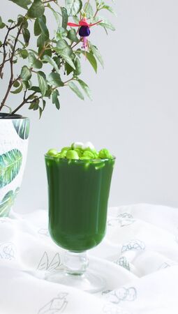 green drink with marshmallows and fuchsia flower in a ceramic pot in the backgroundの写真素材