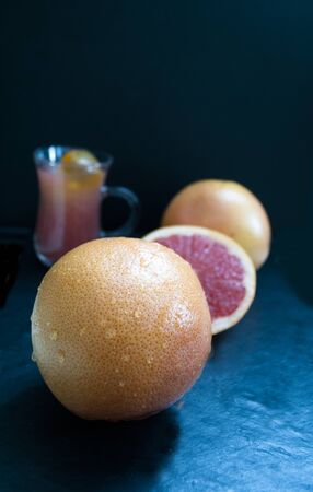 large round whole grapefruit on a dark background with a glass of juiceの写真素材