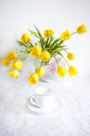 bouquet of yellow tulips in a vase on a white table and a coffee mugの写真素材