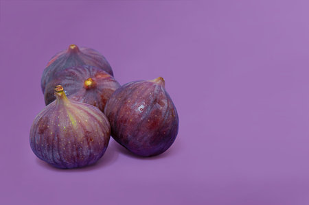figs with wet spots from water on the skin are lying in a pile on a purple backgroundの写真素材