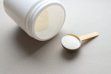 A plastic spoon of collagen powder and a jar on a gray background