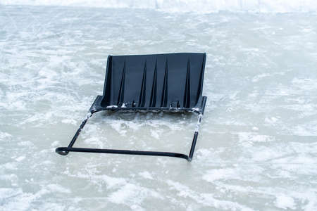 A black plastic wide snow shovel lying on the iceの写真素材