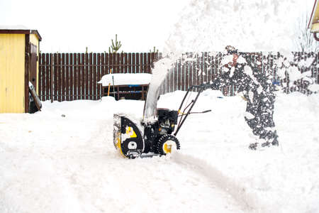 a man removing and cleaning the road from snow with a gasoline snow blowerの写真素材