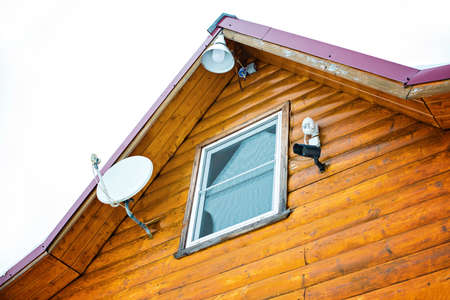 satellite plate, TV antenna, lantern or flashlight and video camera on the roof of a brown wooden houseの写真素材