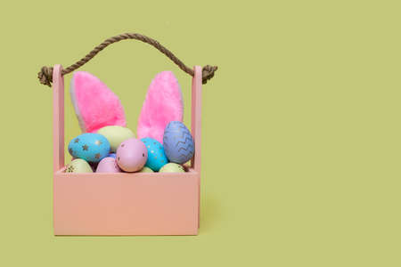 Wooden basket with colored eggs and pink rabbit ears. Easter conceptの写真素材