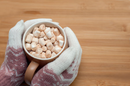 Hands in warm gloves hold a mug with hot chocolate and marshmallows