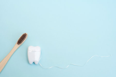 Bamboo toothbrush and white dental floss in the form of a white tooth on a blue background.の写真素材