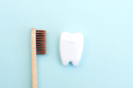 Bamboo toothbrush and white dental floss in the form of a white tooth on a blue background.