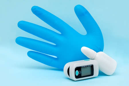 White plastic bottle of medicines, pulse oximeter and medical glove on a blue background.の写真素材