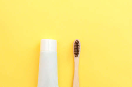 Bamboo toothbrush and tube of paste on a yellow background. Dental care.の写真素材