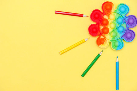 Rainbow color toy anti-stress for fingers Pop It in the shape of a flower on a yellow background....