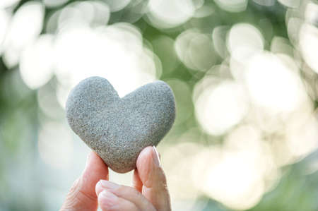 hand holding a heart shaped stone on bokeh backgroundの写真素材
