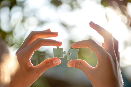 two hands holding puzzle pieces on a bokeh backgroundの写真素材