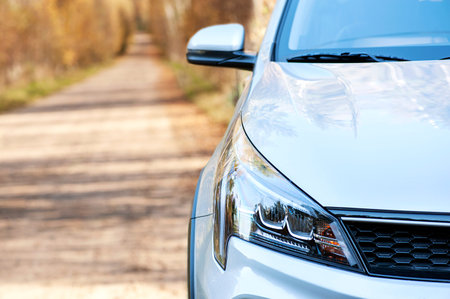 Close-up front view of a car on the background of an autumn forest road. Headlamp glass. Background...