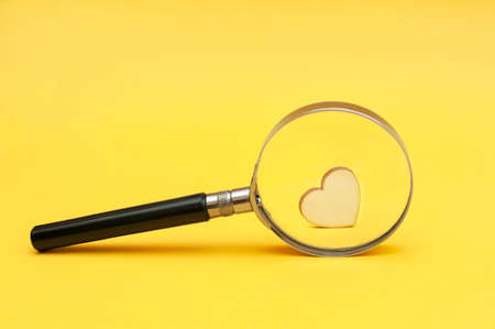 Heart under a magnifying glass on a yellow background.の写真素材