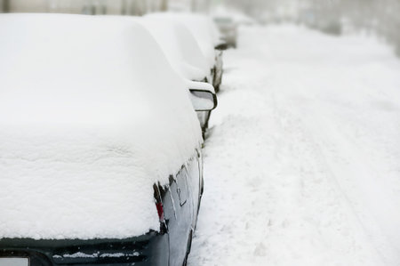 A row of snow-covered cars and a winter road. Copy space. Snowfall