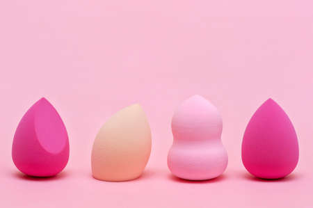 Makeup sponges of different colors and different shapes on a pink backgroundの写真素材
