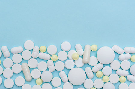Border of scattered medical pills on a blue background with copy space.