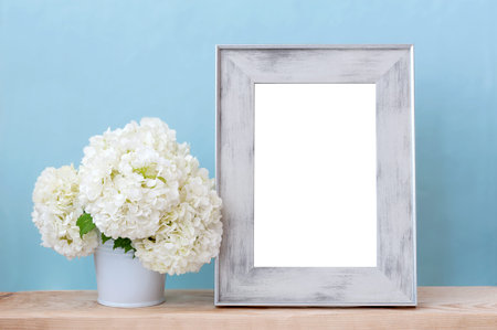 White flowers in a vase and an empty photo frame on a table on a blue backgroundの写真素材