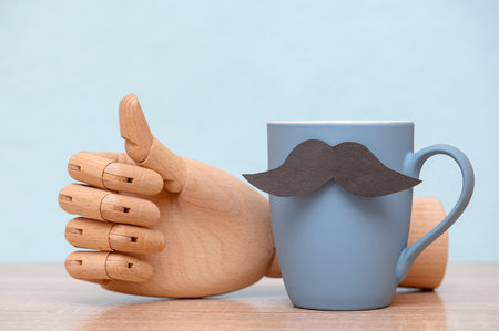 Father's day happy concept with blue mug with mustache, wooden hand with thumb up on tableの写真素材