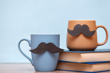 Father's day happy concept with blue and brown mugs with mustache, books on wooden tableの写真素材