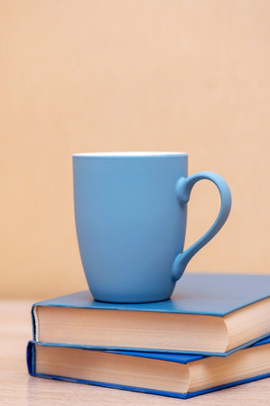 A blue mug and books with a blue hardcover on a wooden table. vertical photoの写真素材