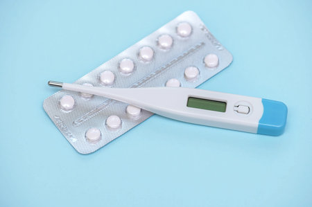 Electronic modern thermometer with pills in a blaster pack on a blue backgroundの写真素材