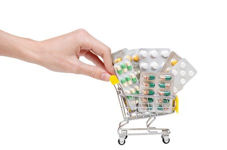 Side view of a person's hand pushing and rolling a mini shopping cart full of pills on a white background. The concept of online medicine stores, online pharmacy.の写真素材