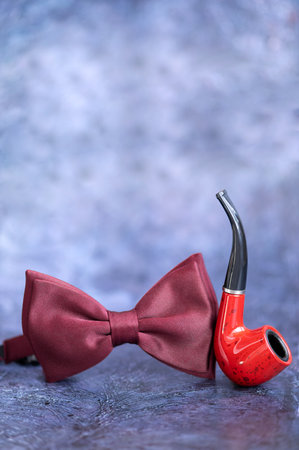Red bow tie and pipe on the table on a blue background. vertical photoの写真素材