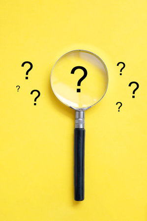 A yellow background with question marks and a magnifying glassの写真素材