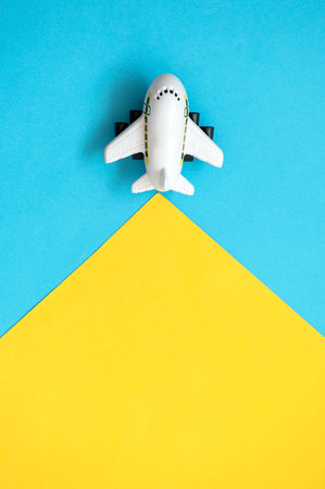 A toy airplane is flying on a yellow and blue background. travel concept. top view.の写真素材