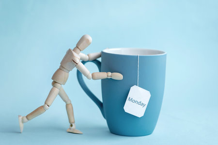 Wooden man pushing a blue cup of tea on a blue background. Blue Monday conceptの写真素材
