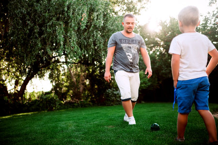 Dad playing football with his son in a green summer garden