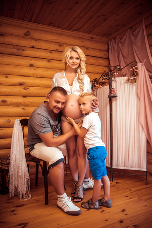 Happy family with a pregnant mother, father and son in a room with wooden wallsの写真素材