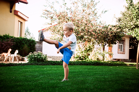 Little blonde boy playing football on the green grass in the summerの写真素材