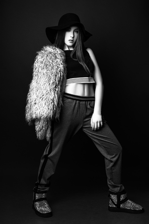 beautiful teenage girl with long hair on a black background. Studio photo. Dressed in gray sports trousers, a tank top and a hat. Black and whiteの写真素材