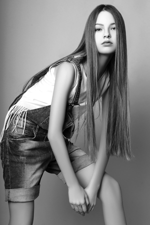 beautiful teenage girl with long hair on a yellow background. Studio photo. Dressed in a white jersey and blue denim overalls. Black and whiteの写真素材