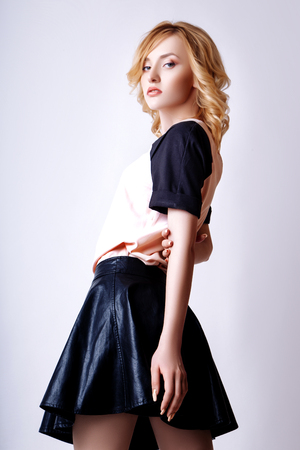 Fashion photo of young curly blonde woman on white background. In a pink shirt with black sleeves and a black leather skirtの写真素材