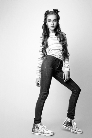 beautiful teenage girl with long curly hair on a white background. Studio photo. Dressed in a blouse in a colorful strip and jeans. Black and whiteの写真素材