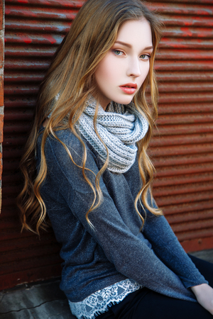Gorgeous fashionable young blonde girl street portrait. Dressed a gray sweater, wide scarf and black trousersの写真素材