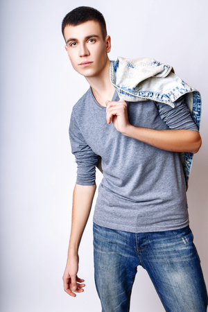 Attractive trendy young man dressed in gray t-shirt, blue denim vest and jeans standing on white background. Studio photo.の写真素材