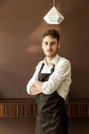 A handsome male jeweler in an apron and shirt in thought before starting workの写真素材