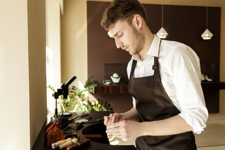 A handsome male jeweler is looking at the ring. Workplace. Jewelery Makingの写真素材