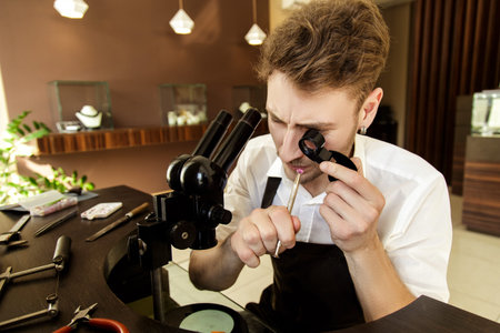 handsome guy jeweler examines a pink gemstone through a magnifying glass in the process of creating...