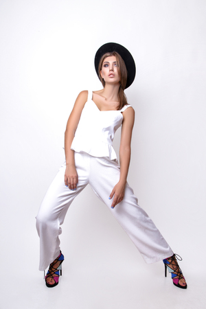 Posing gorgeous emotional girl in a white suit and black hat in the studio on a white background.の写真素材