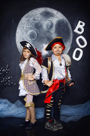 Little boy and girl dressed in pirate costumes on a black background with a moon image in a studio with Halloween decorationsの写真素材