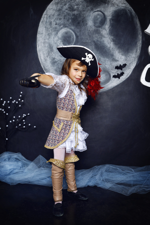 Little girl dressed in pirate costume on a black background with a moon image in a studio with Halloween decorationsの写真素材