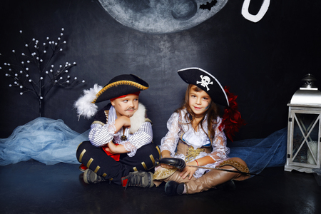 Little boy and girl dressed in pirate costumes on a black background with a moon image in a studio with Halloween decorationsの写真素材